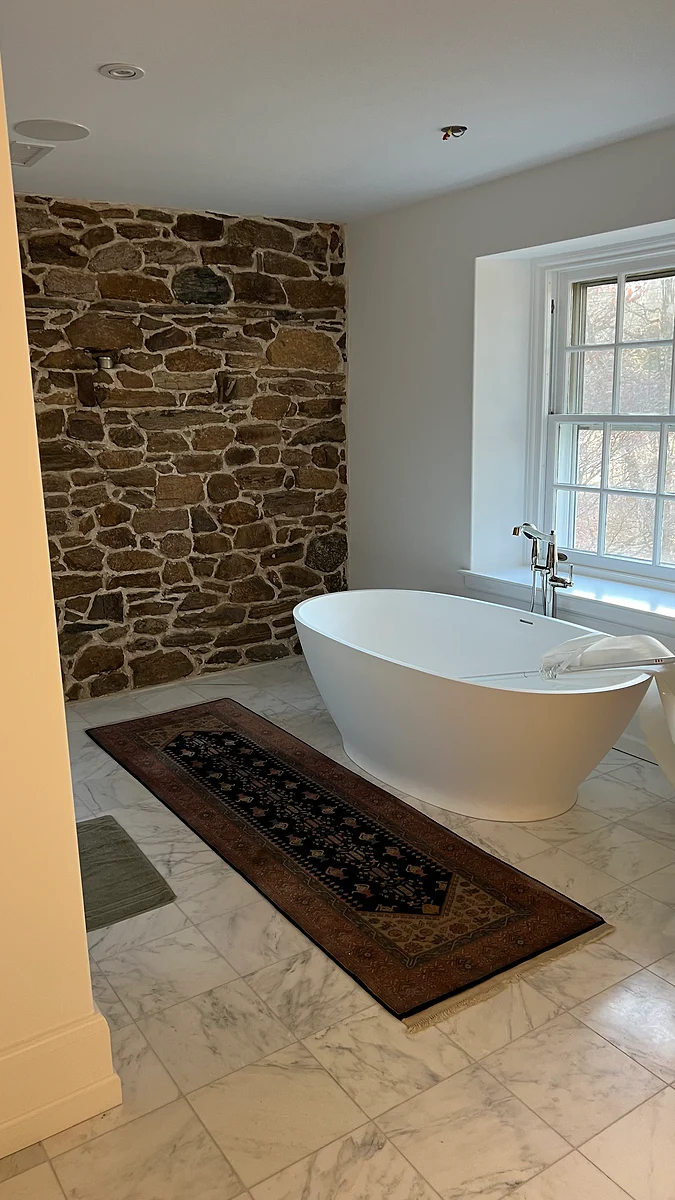 Renovated bathroom with a freestanding tub and preserved stone wall